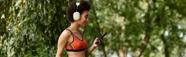 Una donna che usa smartphone e ascolta musica in cuffia circondata da alberi vibranti e aria fresca. — Foto stock