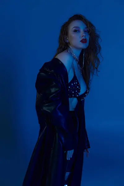 A confident woman showcases her fashion sense in a bold, blue lit setting. — Stock Photo
