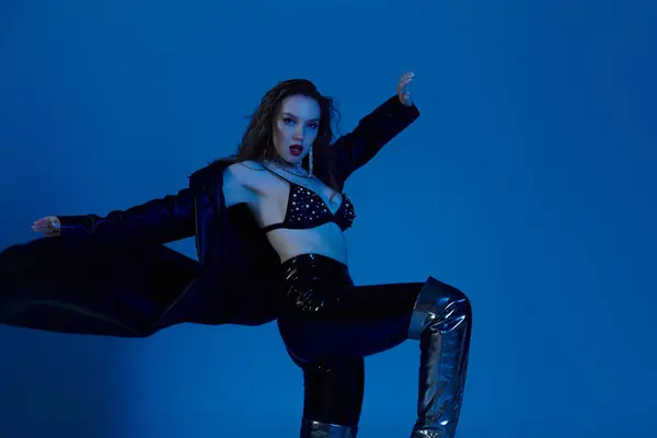A striking red haired woman confidently poses in fashionable attire against a blue backdrop. — Stock Photo