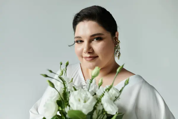 Una splendida sposa plus size mette in mostra l'eleganza in un abito da sposa bianco e splendidi orecchini mentre tiene fiori freschi. — Foto stock