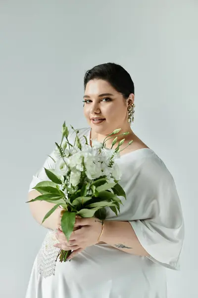 Una splendida sposa plus size tiene un mazzo di fiori freschi, incarnando la grazia in un abito bianco. — Foto stock