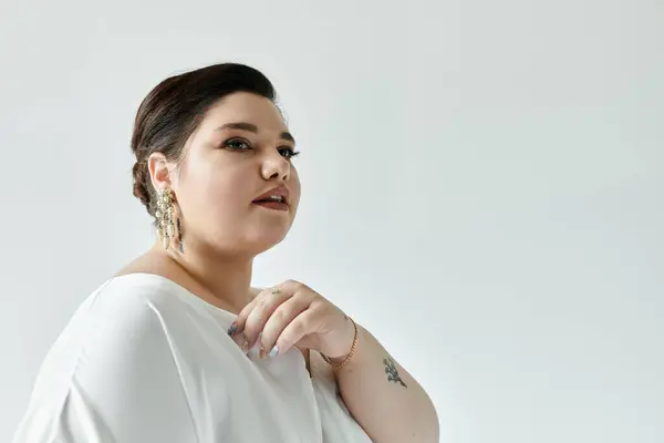 A stunning plus size bride radiates elegance in a white gown and sparkling earrings, set against a grey background. — Stock Photo