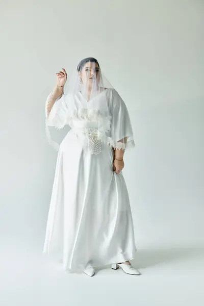 Eine wunderschöne Braut in einem fließenden weißen Kleid präsentiert ihre strahlende Eleganz vor einem dezenten grauen Hintergrund. — Stockfoto