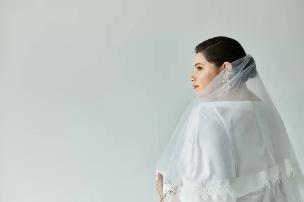 A stunning bride in a white gown and elegant earrings radiates beauty on a soft grey background. — Stock Photo