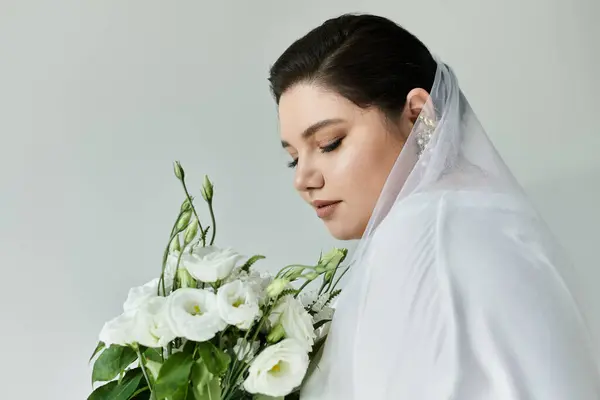 Une superbe mariée de plus de taille dans une robe blanche regarde attentivement tout en saisissant un bouquet de fleurs blanches. — Photo de stock