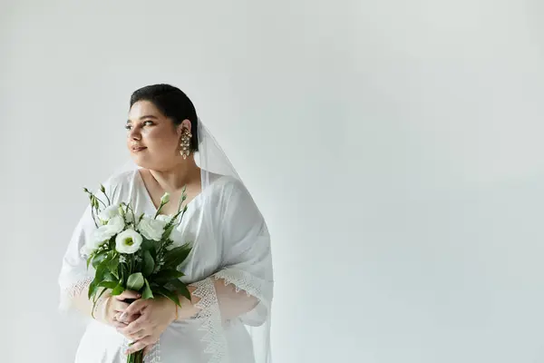 A radiant bride in a white gown and veil gently holds a bouquet, exuding beauty and grace. — Stock Photo