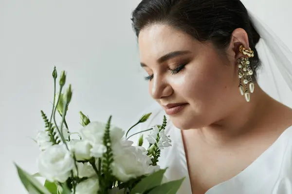 A beautiful young bride in a white gown gently holds a bouquet while showcasing her stunning earrings. — Stock Photo
