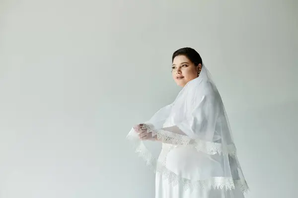 A radiant young bride in a flowing white gown and earrings, exuding joy against a serene grey backdrop. — Stock Photo
