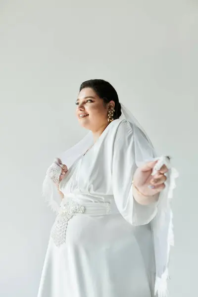 A beautiful young bride beams in a white gown with earrings, radiating joy against a grey backdrop. — Stock Photo