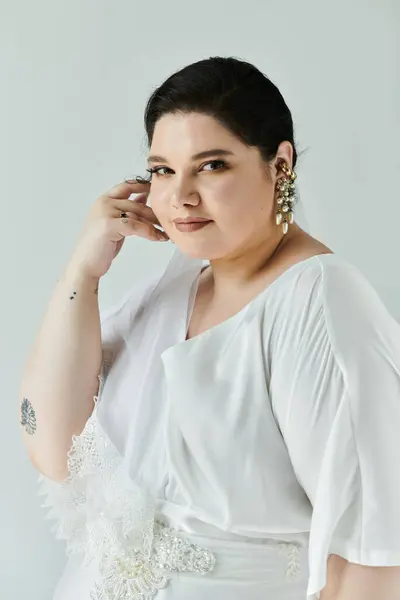 Una hermosa novia de talla grande muestra su vestido de novia blanco y pendientes, exudando confianza y gracia. - foto de stock