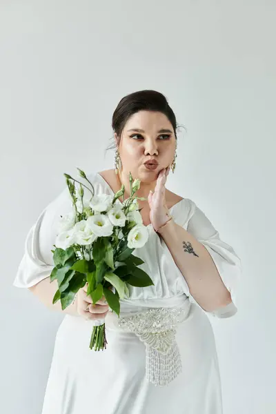 Впевнена наречена в білій сукні грайливо позує з букетом, демонструючи красу і елегантність. — стокове фото