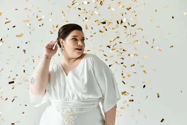 A stunning young woman in a flowing white wedding dress shines amidst sparkling gold confetti. — Stock Photo