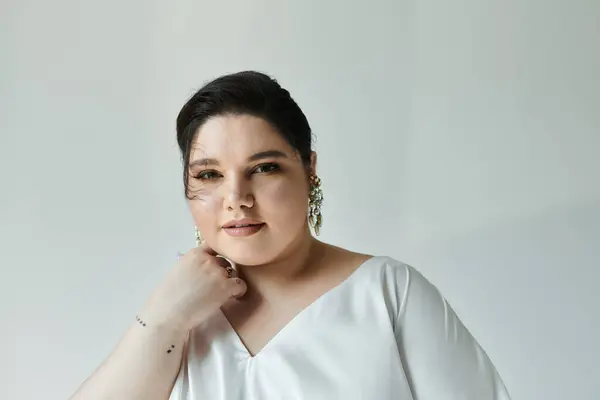 A stunning plus size bride exudes elegance in a white gown and striking earrings on a subtle grey background. — Stock Photo