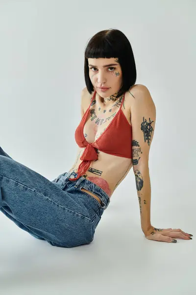 A stylish woman showcases her tattoos while sitting against a clean backdrop. — Stock Photo