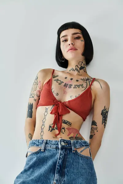 A stylish woman confidently displays her tattoos and outfit against a plain backdrop. — Stock Photo