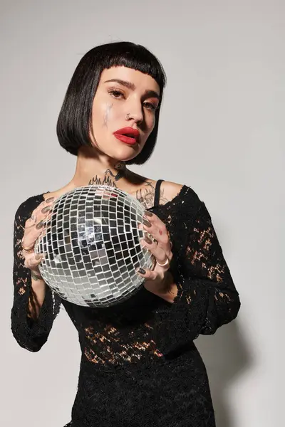 Eine stylische Frau mit Tätowierungen hält eine schimmernde Discokugel in der Hand, bereit für eine Nacht voller Spaß. — Stockfoto