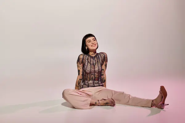 A fashionable young woman showcases her tattoos while sitting playfully. — Stock Photo