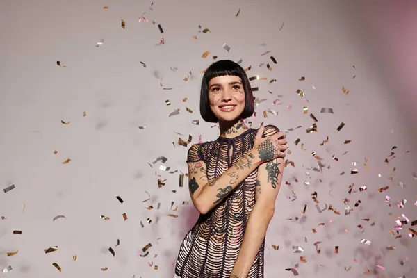 A stylish young woman smiles brightly while surrounded by colorful confetti. — Stock Photo