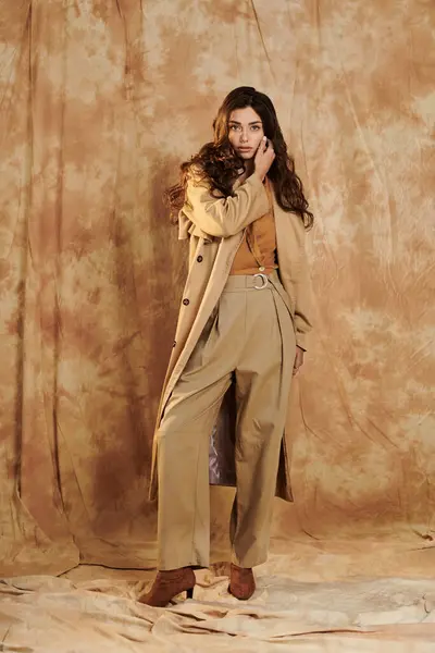 A young woman poses gracefully in a chic autumnal outfit, surrounded by warm, earthy studio backdrops that enhance her style. — Stock Photo