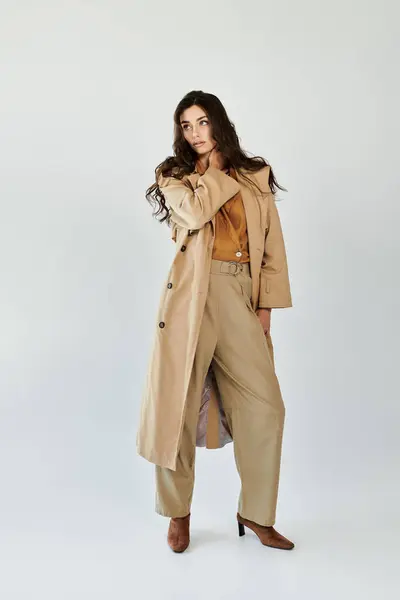 Una giovane donna modella un abito autunno chic, con un elegante trench e pantaloni su misura, trasudando eleganza in uno studio. — Foto stock