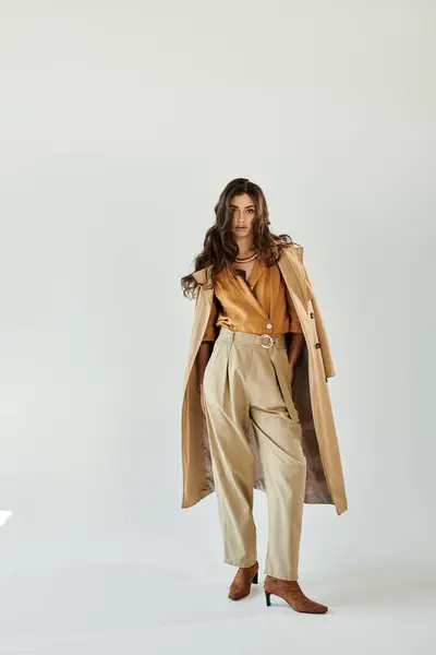 In a serene studio, a beautiful young woman confidently models her chic autumn attire, embodying seasonal elegance. — Stock Photo