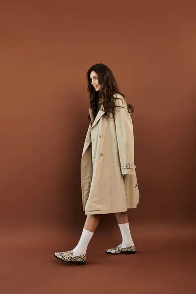 Una mujer joven y hermosa posa elegantemente en un traje de otoño de moda, capturando la elegancia estacional en un estudio. - foto de stock