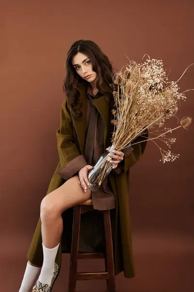 Habillée d'une tenue d'automne chic, une jeune femme respire la beauté et l'élégance tout en tenant des plantes décoratives dans un studio. — Photo de stock