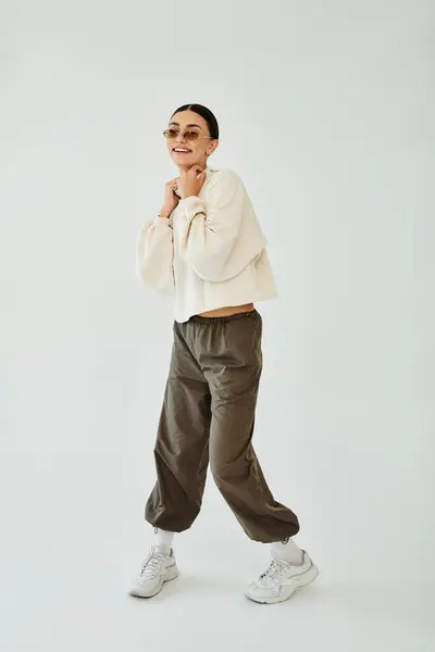 A cheerful young woman showcases her stylish autumn outfit while posing confidently in a bright studio environment. — Stock Photo
