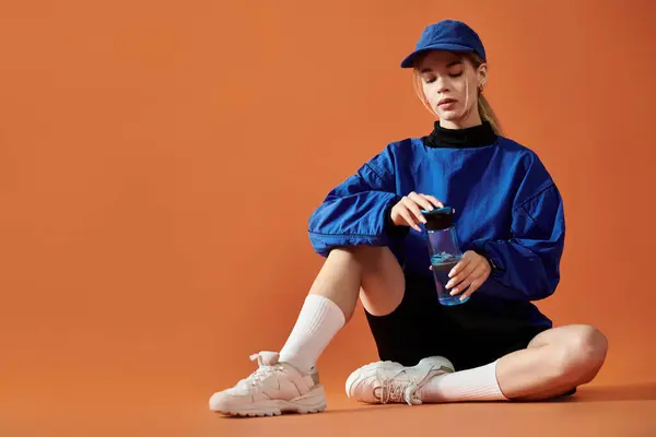 A stunning athlete shares her feelings while sipping a drink in sporty gear against a bold backdrop. — Stock Photo