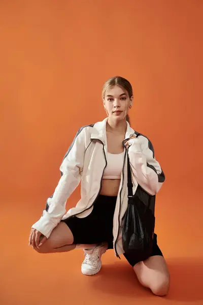 A powerful sportswoman kneels in a striking orange background, radiating determination and emotion. — Stock Photo