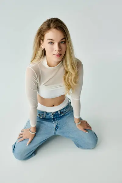 A beautiful woman with long hair kneels in casual attire against a minimalist backdrop. — Stock Photo