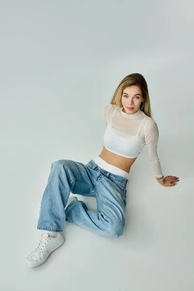 A young woman in light attire poses elegantly on a soft surface, radiating confidence. — Stock Photo