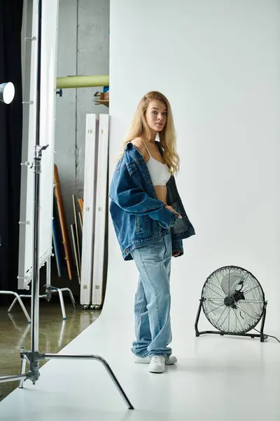 A stylish woman in a denim outfit stands confidently in a studio. — Stock Photo