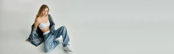 A young woman relaxes on the floor, flaunting her stylish denim outfit and natural beauty. — Stock Photo