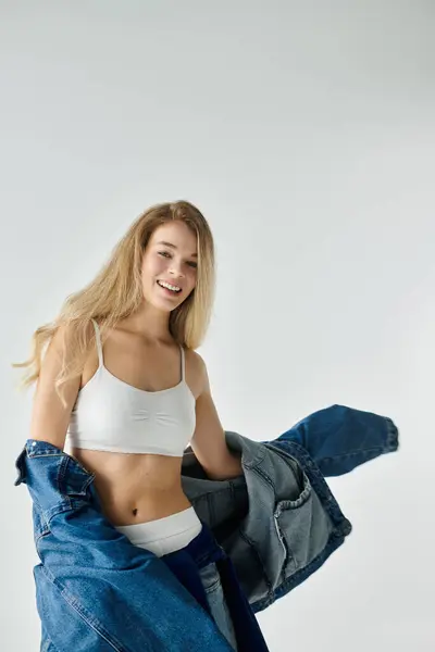 Une jeune femme aux cheveux fluides pose joyeusement dans une veste en denim élégant et haut blanc. — Photo de stock