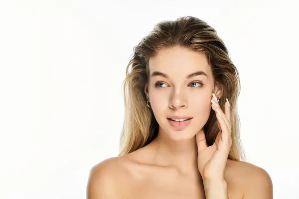 La joven se toca la cara suavemente, mostrando su belleza natural y rasgos suaves. - foto de stock