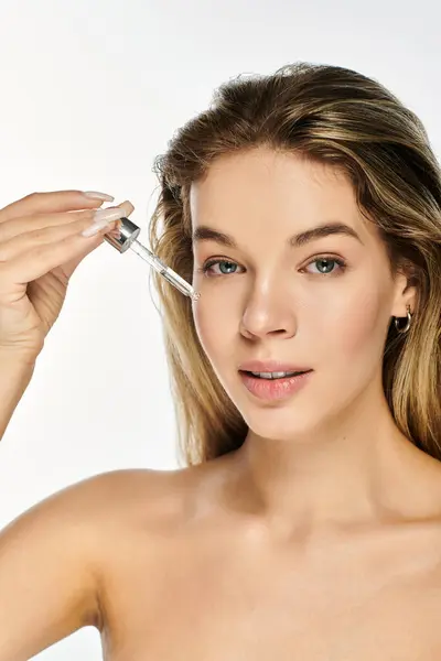 A young woman gently applies serum to her glowing skin, radiating youthful beauty and confidence. — Stock Photo