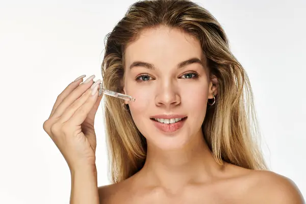 A young woman smiles confidently while applying a skin serum to enhance her natural beauty. — Stock Photo