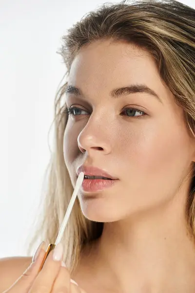 A lovely young woman enhances her lips with gloss, radiating confidence in a serene setting. — Stock Photo