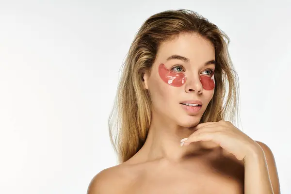 This beautiful young woman enjoys a self care moment, applying eye masks for rejuvenation. — Stock Photo