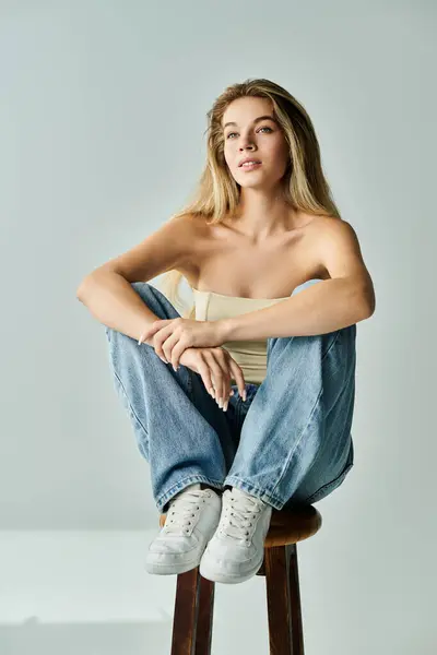 A young woman with flowing hair sits on a stool, exuding confidence and beauty in her pose. — Stock Photo