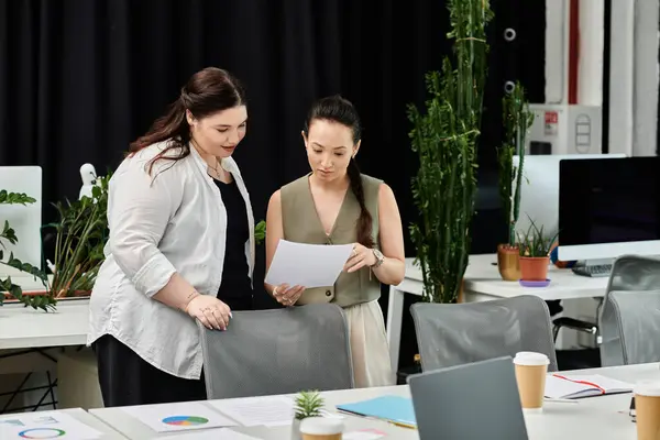 Two professional women in an office discuss important documents while surrounded by greenery. — Stock Photo
