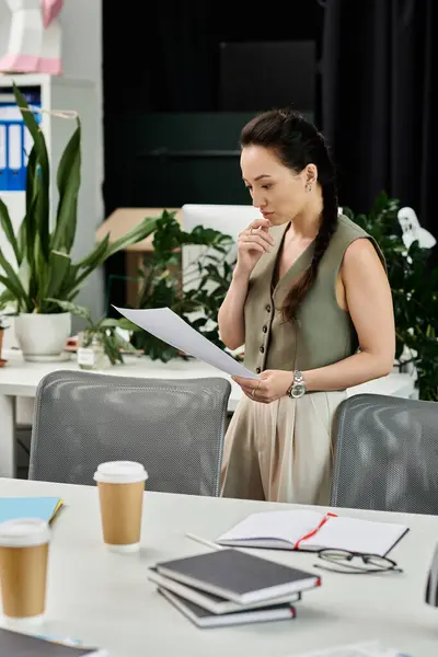 A professional woman thoughtfully examines papers in a stylish office adorned with greenery. — Stock Photo