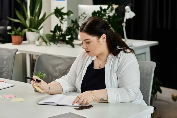 A professional woman writes notes and reviews her ideas in a chic office space filled with greenery. — Stock Photo