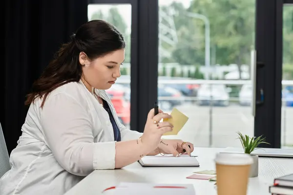 A focused professional outlines her ideas and notes diligently in a well designed office space. — Stock Photo