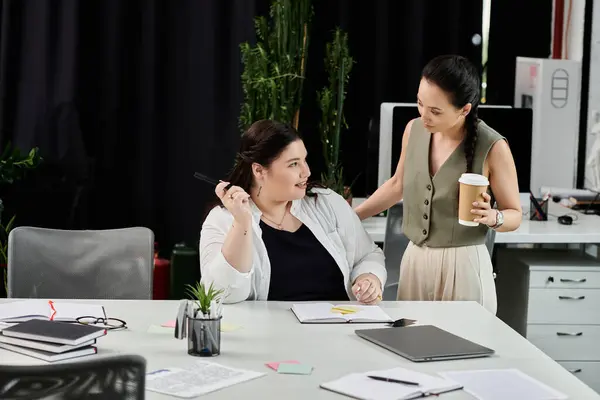 Two professional women collaborate over notes and coffee in a modern office setting. — Stock Photo