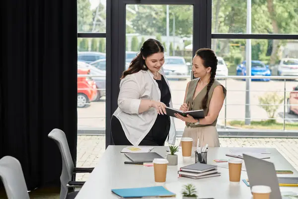 Two professional women discuss ideas while reviewing documents in a bright office space. — Stock Photo