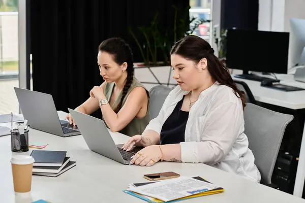 Dos profesionales se centran en sus computadoras portátiles, compartiendo ideas en un ambiente de oficina elegante. - foto de stock