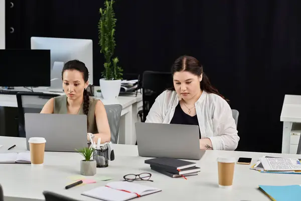 Two professional women focus intently on their laptops while seated at a chic office desk. — Stock Photo