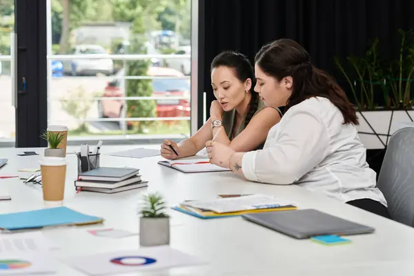 Two professional women engaged in a thoughtful discussion while reviewing documents at a desk. — Stock Photo